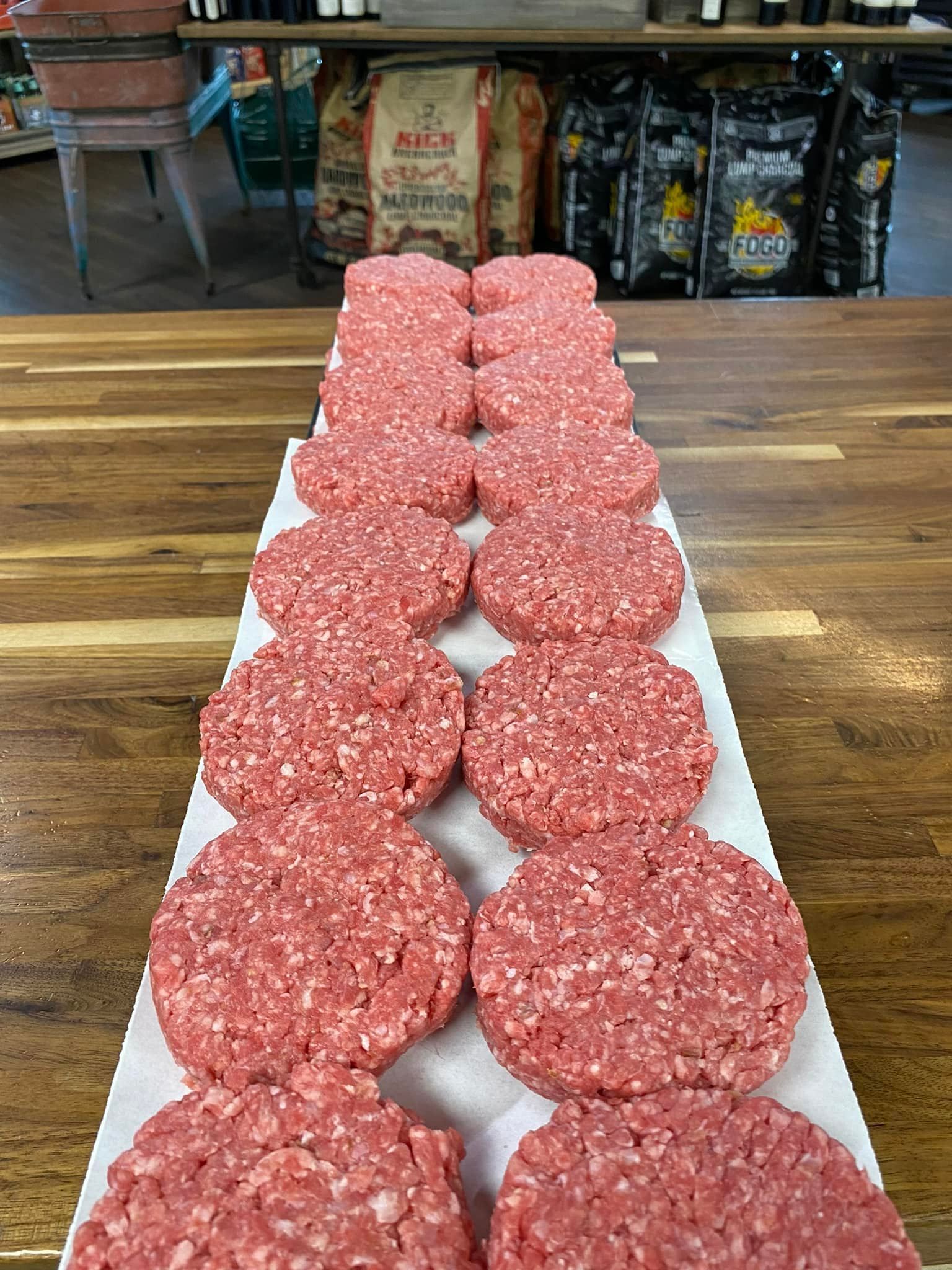 Raw hamburger patties arranged on a white surface, likely in a butcher shop or grocery store.