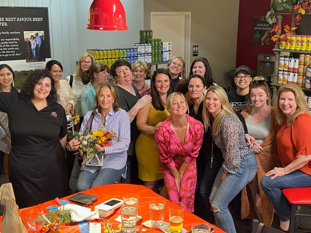 Group of women smiling, posing indoors near food displays.