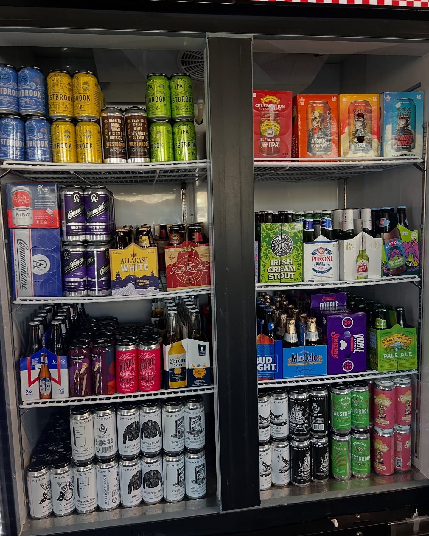 A refrigerator stocked with various canned and bottled beers, displayed on shelves.