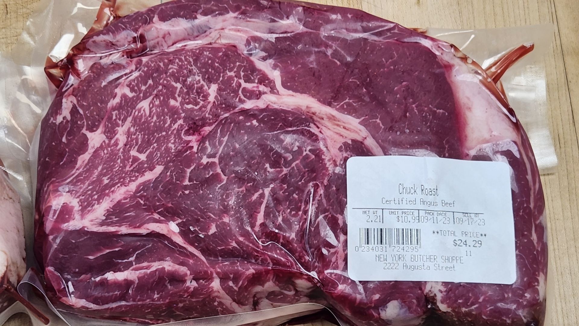 Close-up of raw ribeye steak in plastic packaging, with fat marbling.