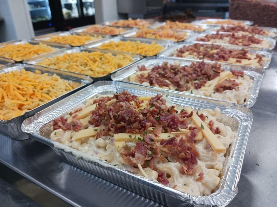 Rows of macaroni and cheese trays, some with bacon, cheese, and herbs.