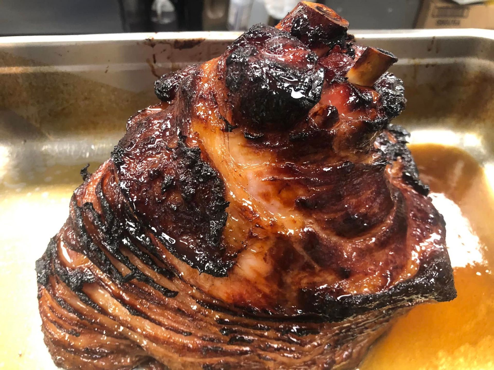 Roasted ham in a baking dish, glazed with a dark, glossy crust.