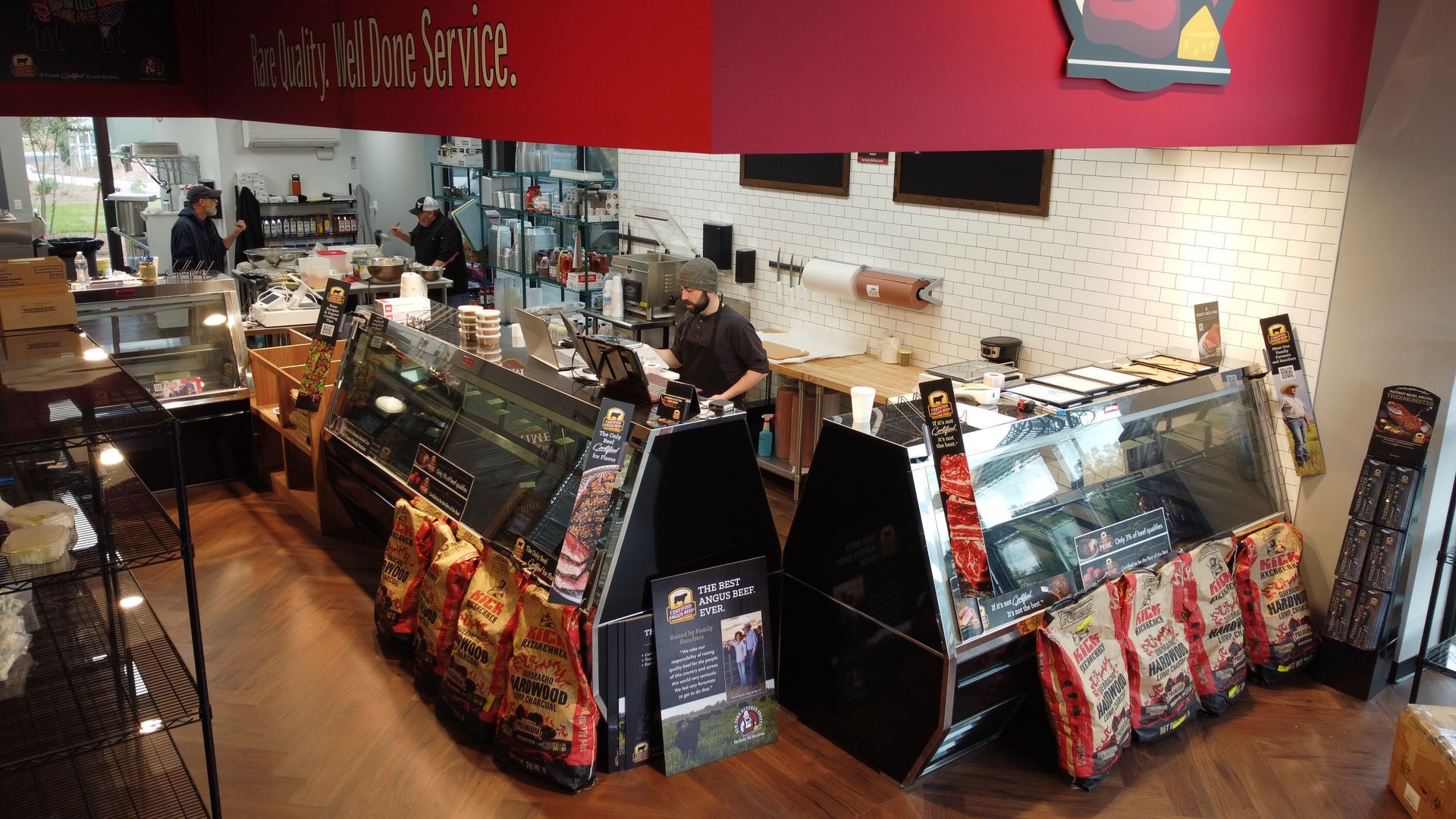 Inside a deli; employees behind glass counters, various food items displayed, red and white interior.