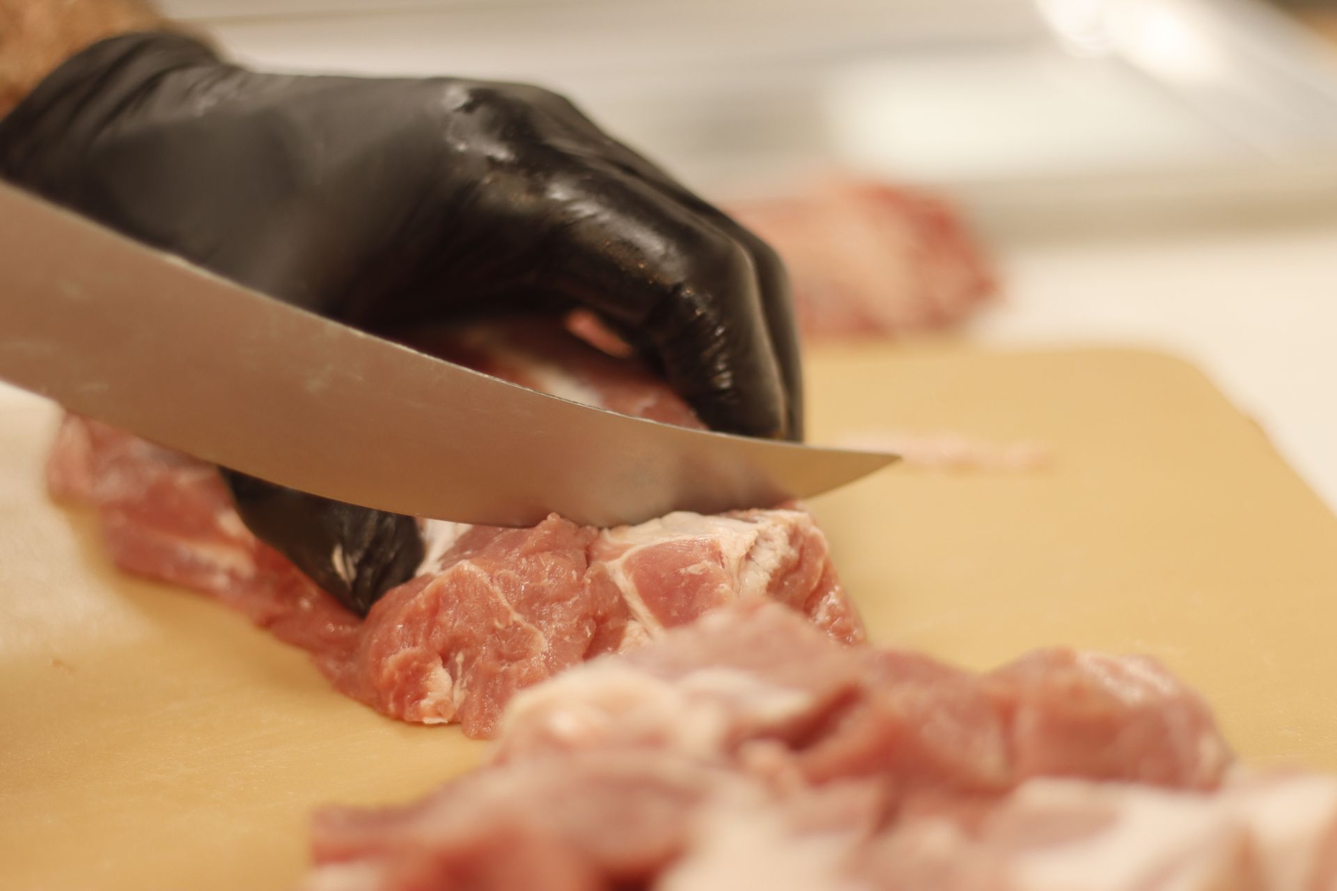 Hand in black glove slicing raw meat on a cutting board.