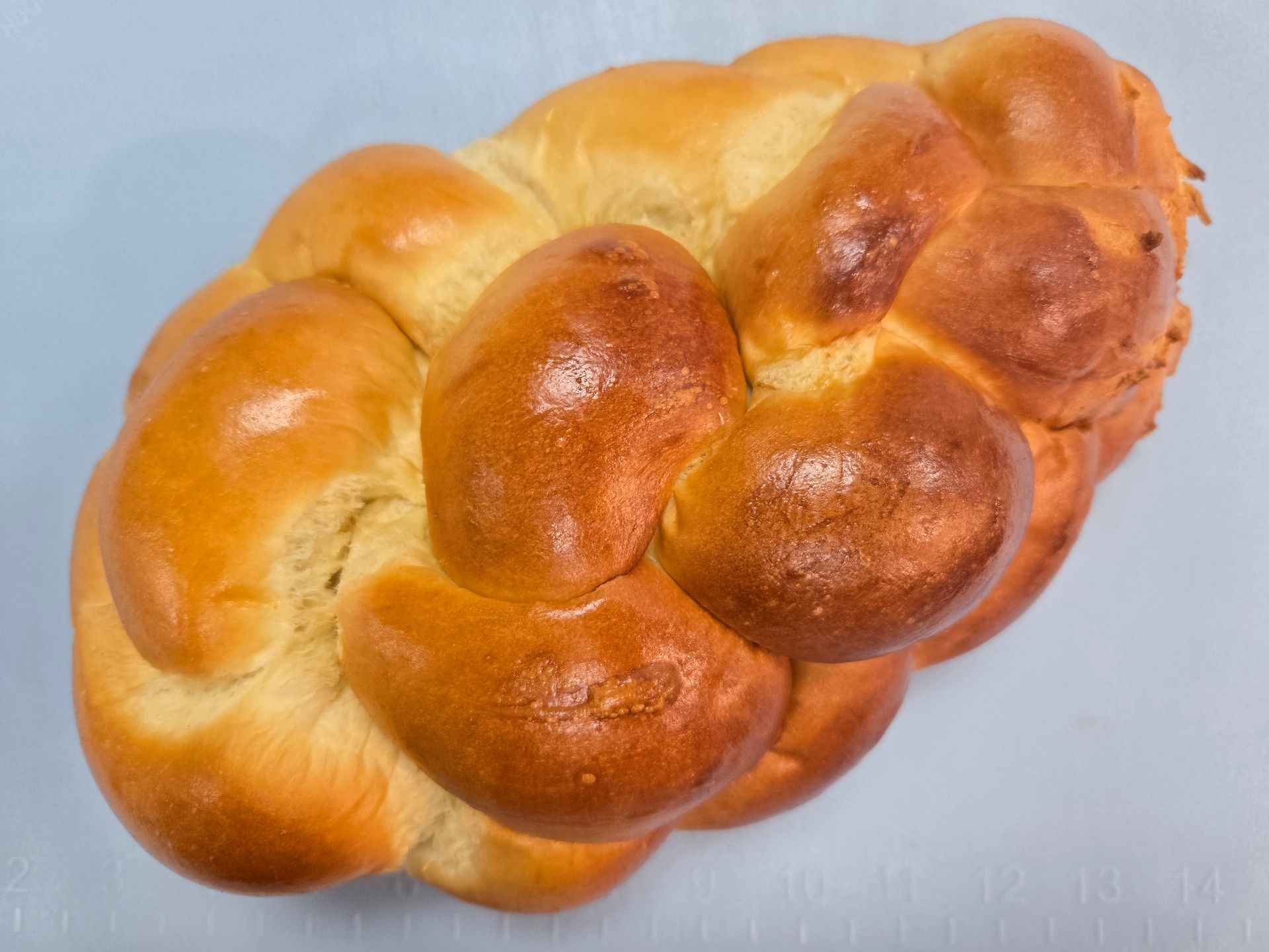 Golden, braided challah bread loaf on a light blue surface.