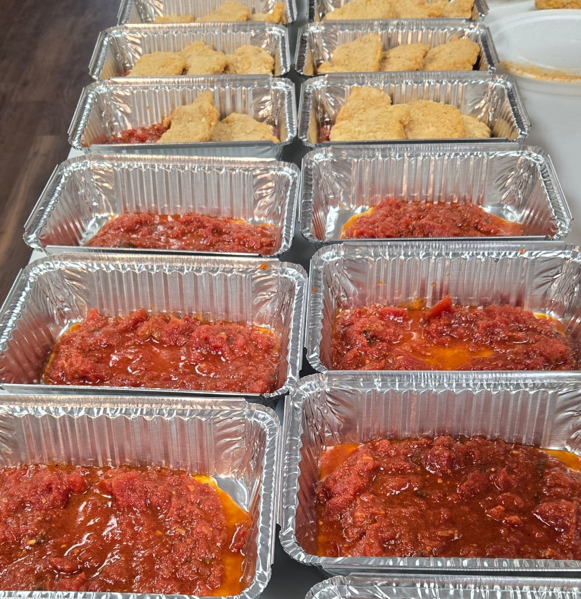 Aluminum trays filled with layers of food: sauce, then breaded pieces.