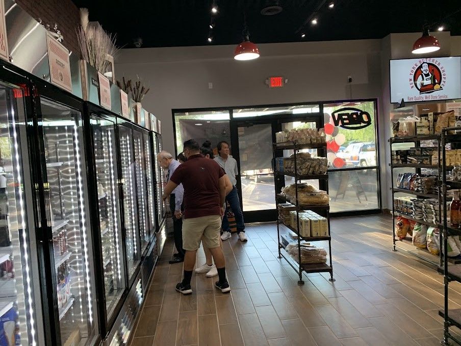 People browsing products inside a shop with refrigerated displays, wood floors, and a sign on the wall.