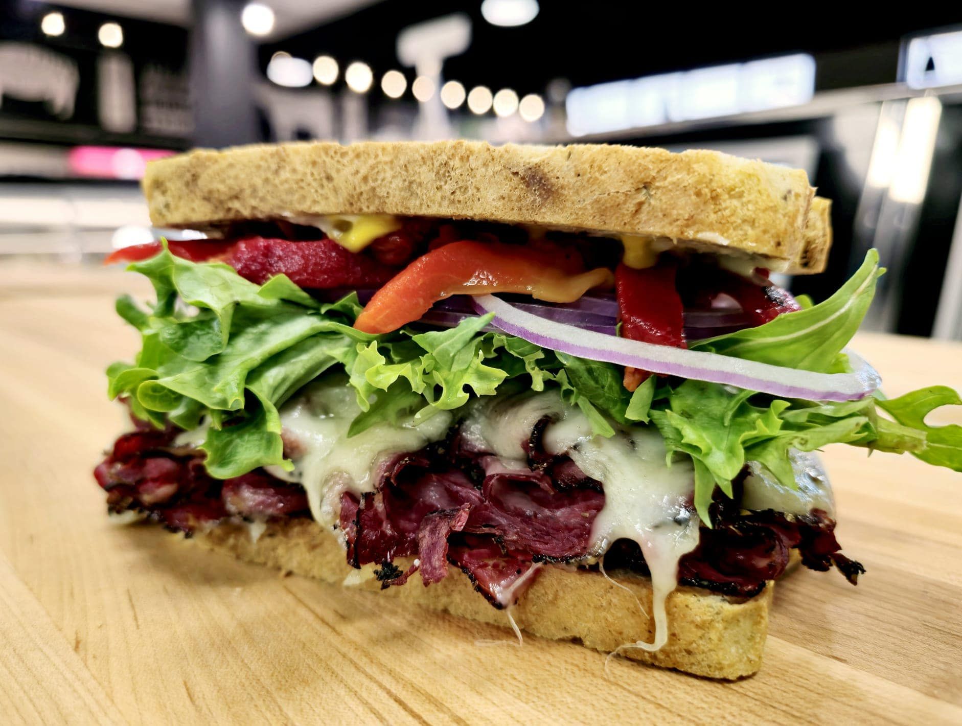 Pastrami sandwich with lettuce, onion, and peppers on wood.