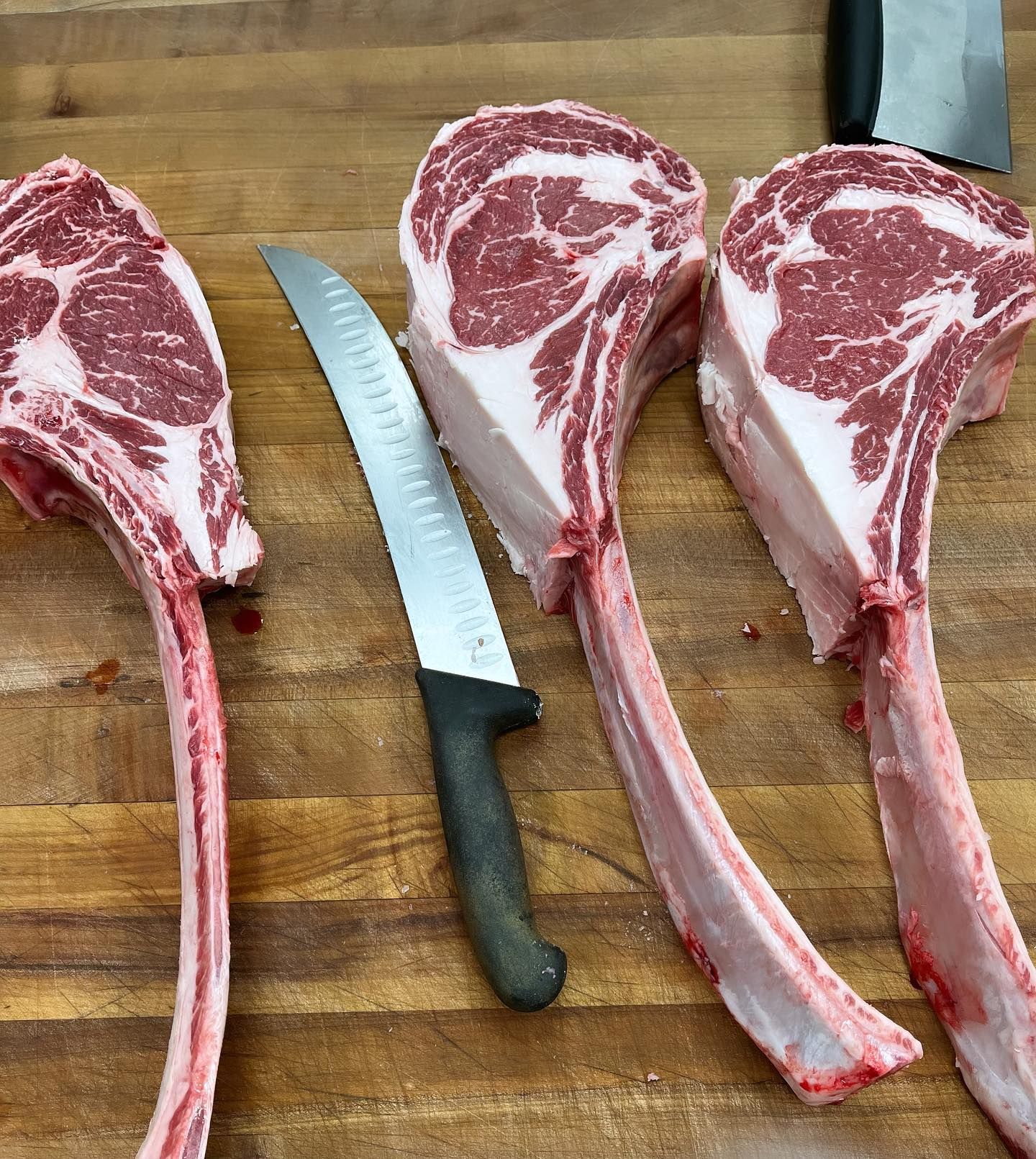 Three bone-in ribeye steaks with a knife on a wooden butcher block.
