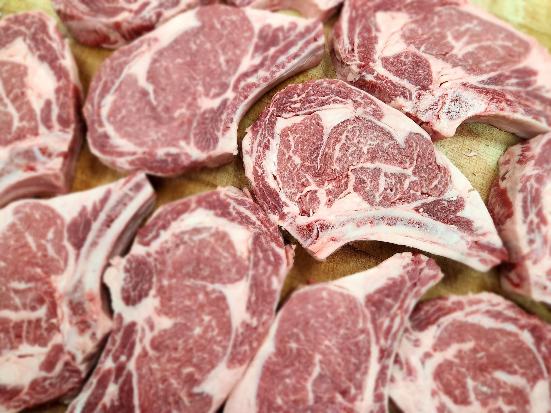 Raw pork chops, red and white, piled on a cutting board.
