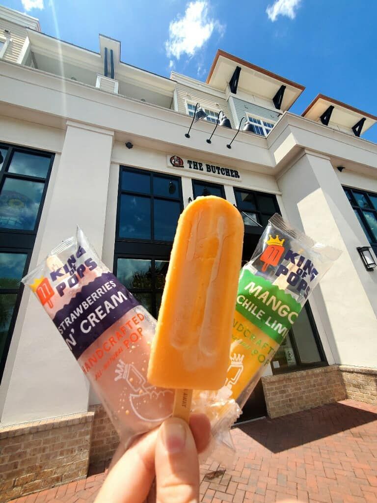 Hand holding three King of Pops: mango, strawberry cream, and mango chile lime, in front of a building.