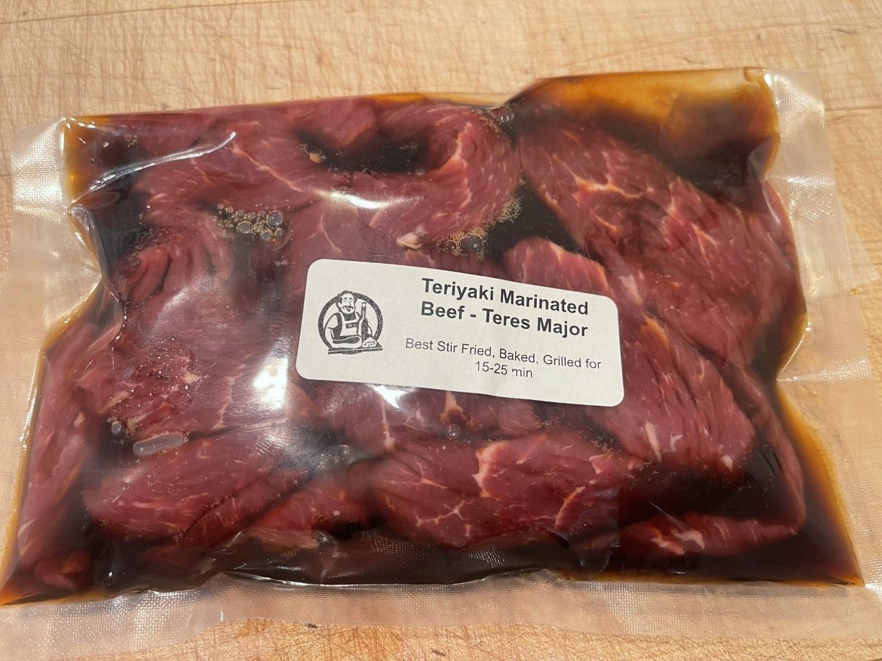 Sealed package of teriyaki-marinated beef strips, with a label, on a wooden surface.