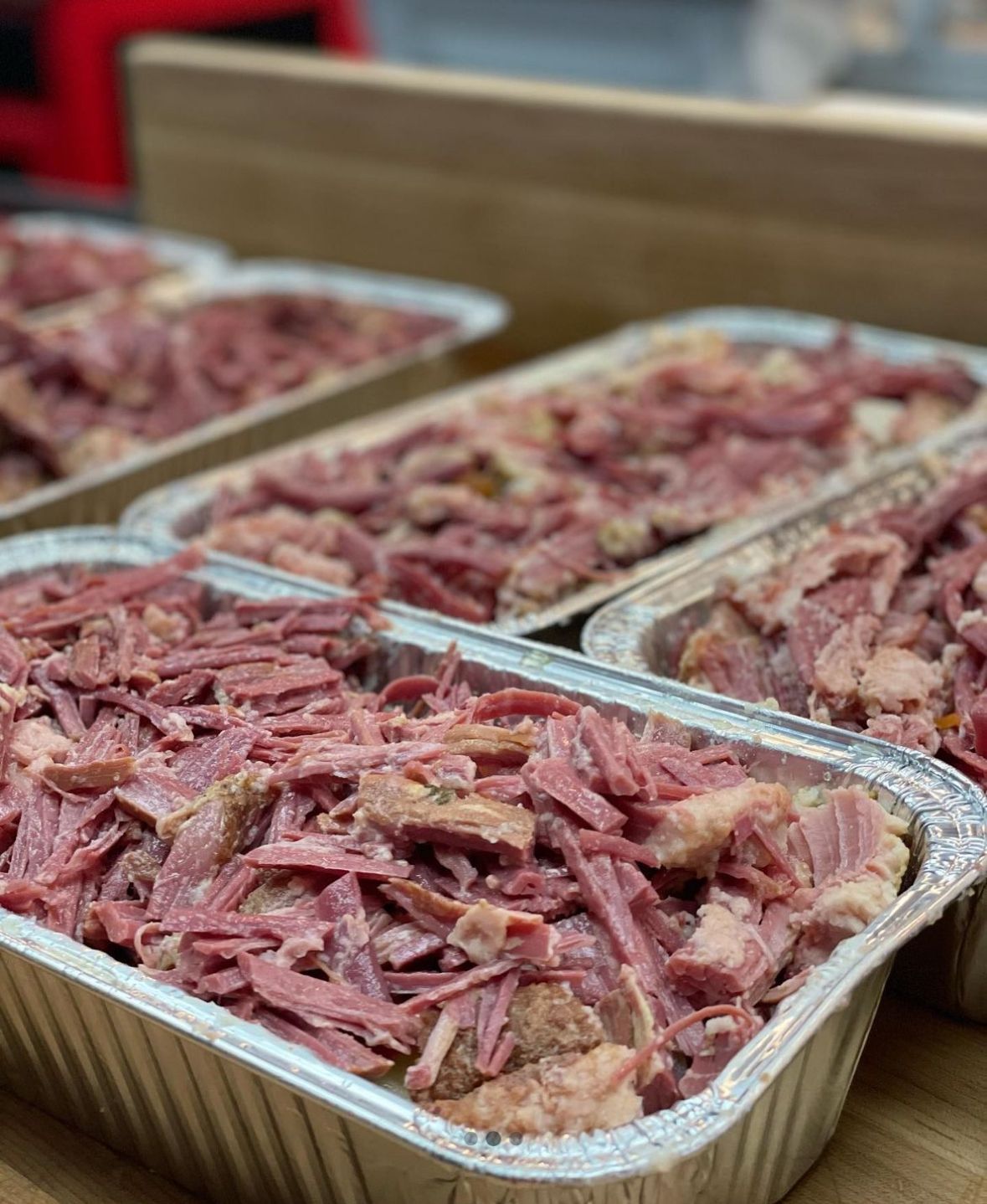 Several aluminum foil trays filled with shredded cooked corned beef, ready to serve.