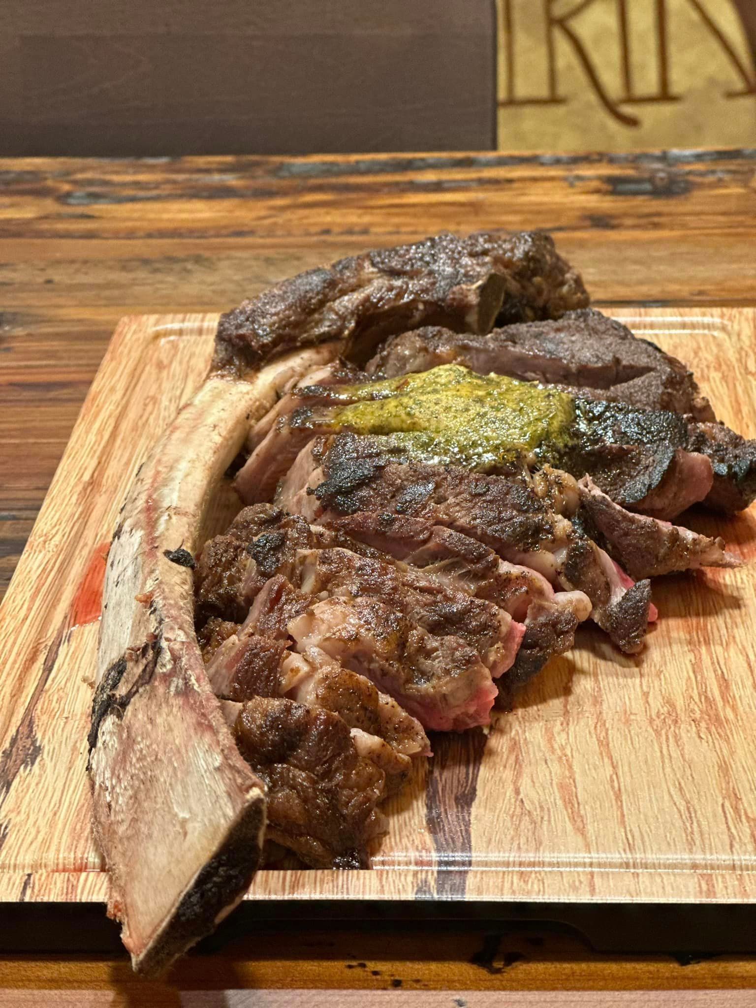 Sliced steak with bone-in, on a wooden cutting board, topped with green sauce.