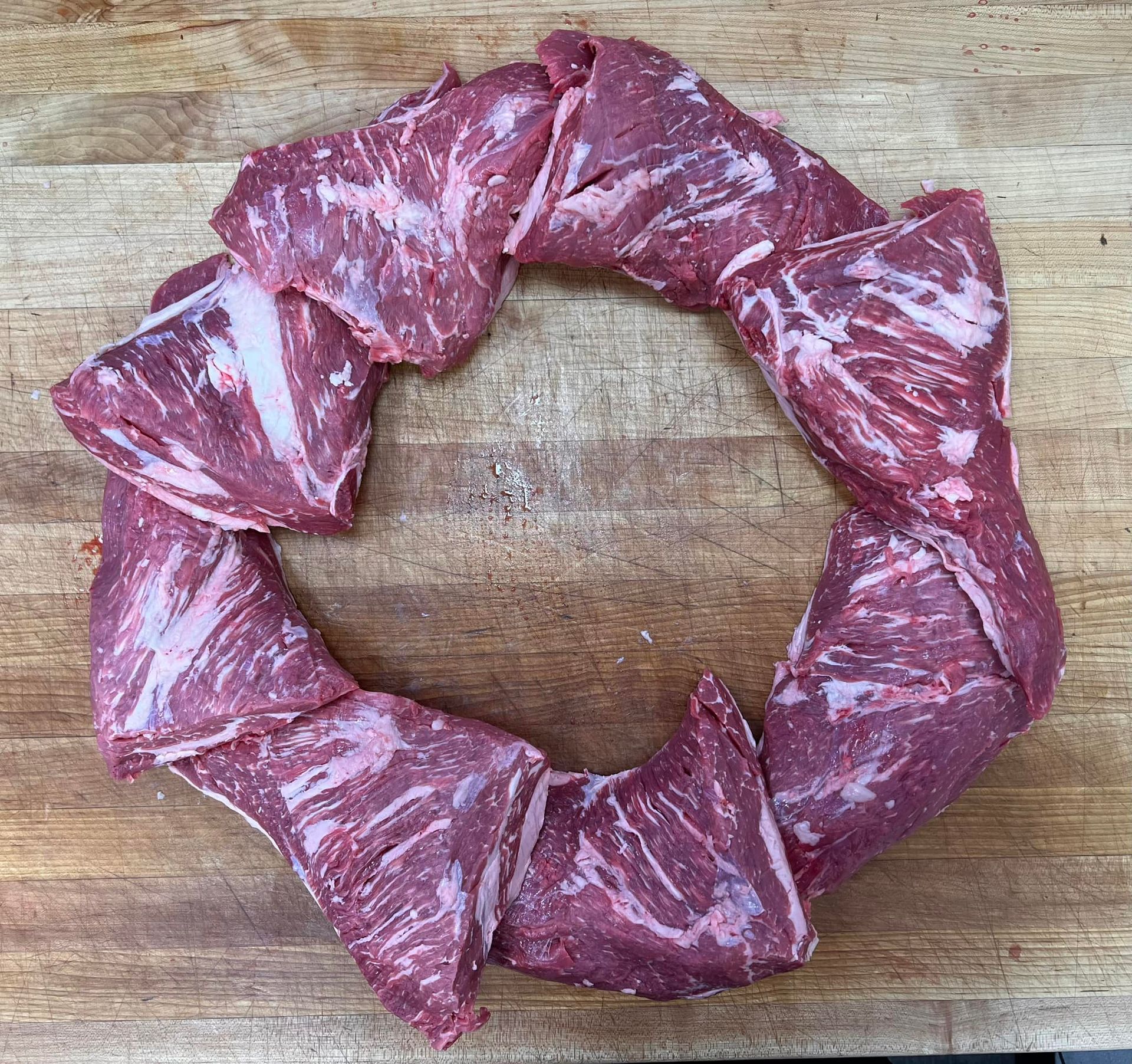 Raw beef slices arranged in a circle on a wooden cutting board.