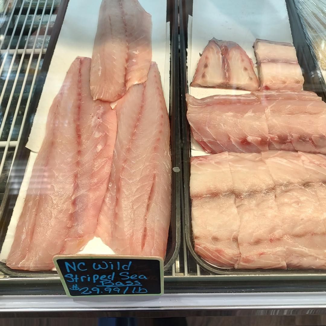 Fresh, raw NC Wild Striped Sea Bass fillets in a seafood display case.
