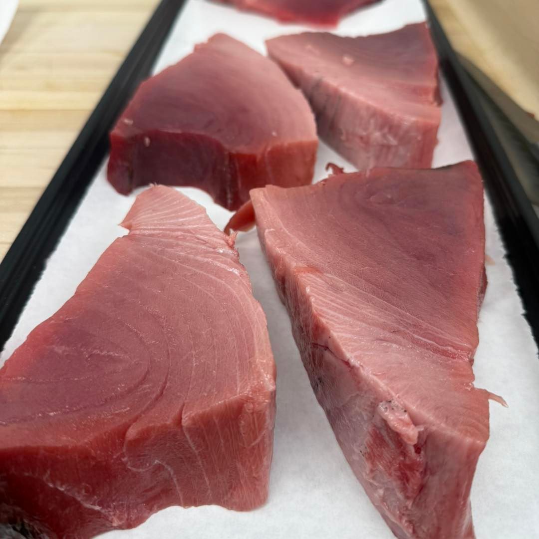Raw tuna steaks, deep red color, arranged on white paper in a tray.