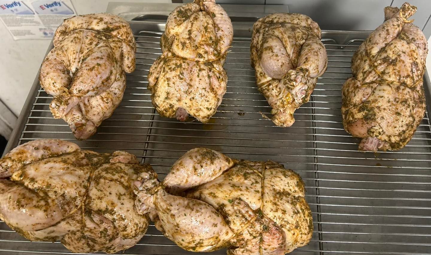 Seven seasoned raw chickens arranged on a metal wire rack, ready for cooking.