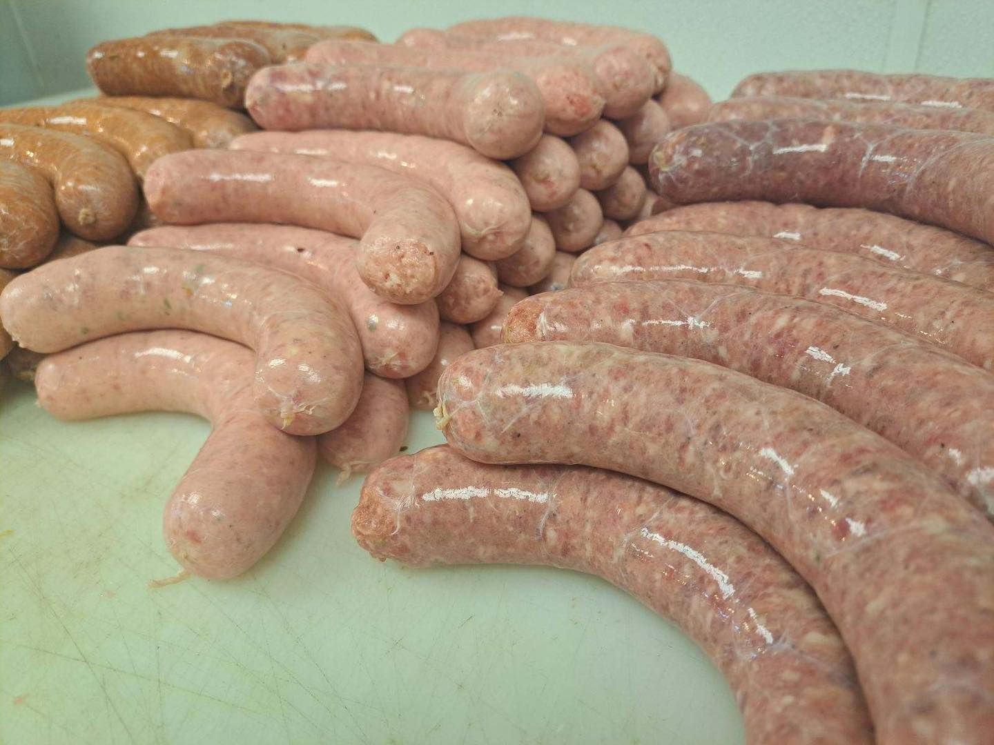 Various raw sausages in different colors piled on a white surface.