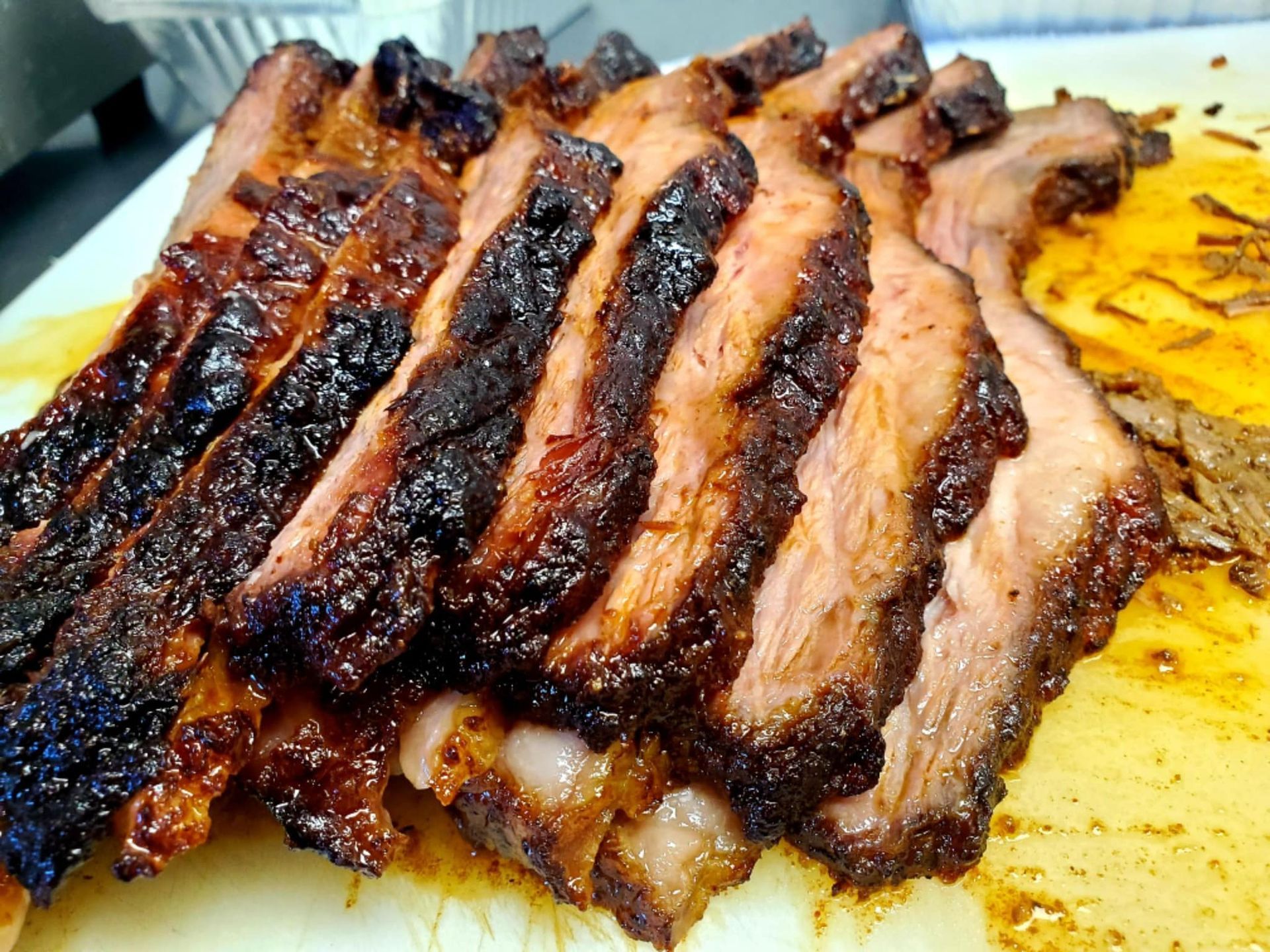 Sliced smoked brisket, dark crust, juicy pink interior, on a cutting board.