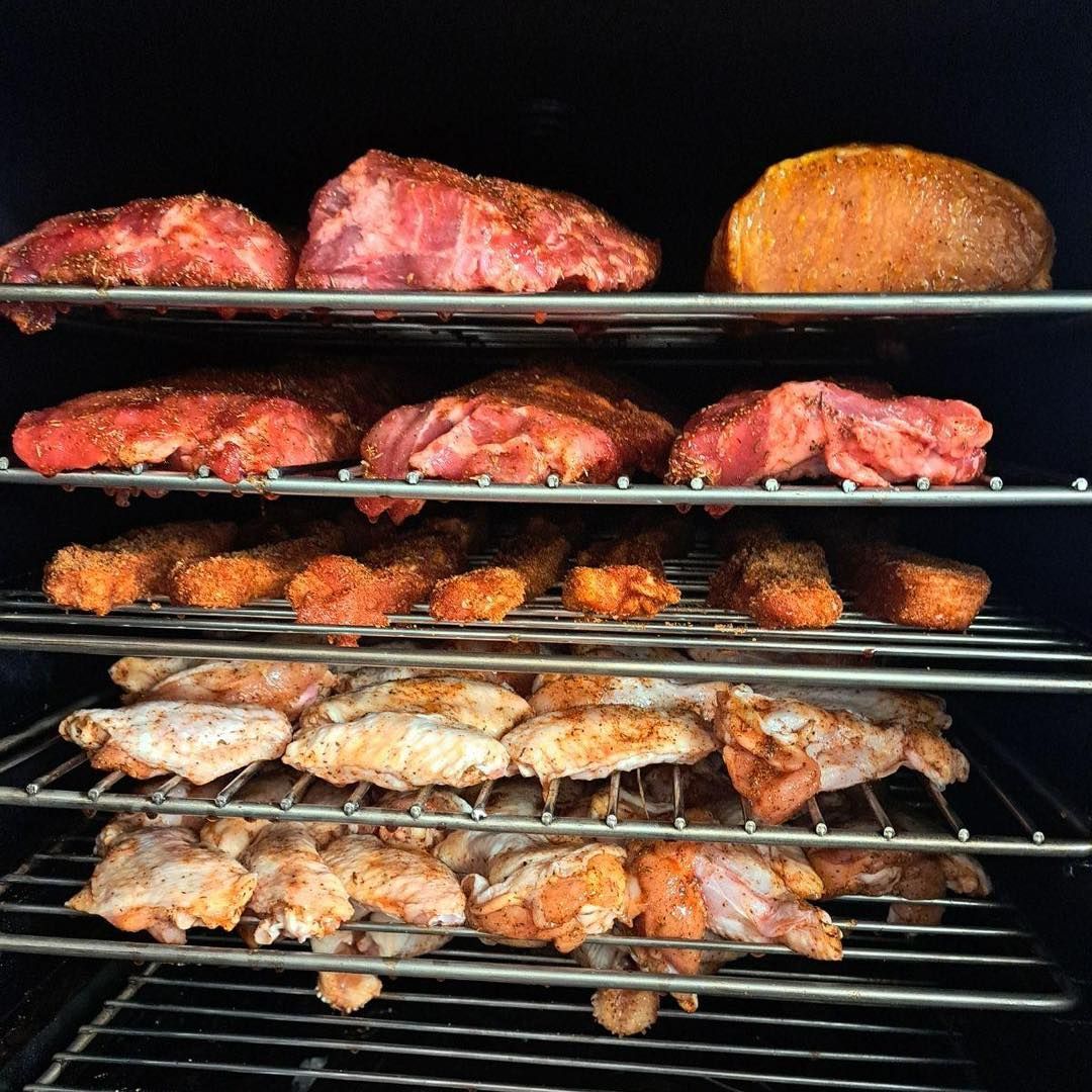 Smoker filled with rows of seasoned meats: pork, chicken wings, and a loaf of bread.