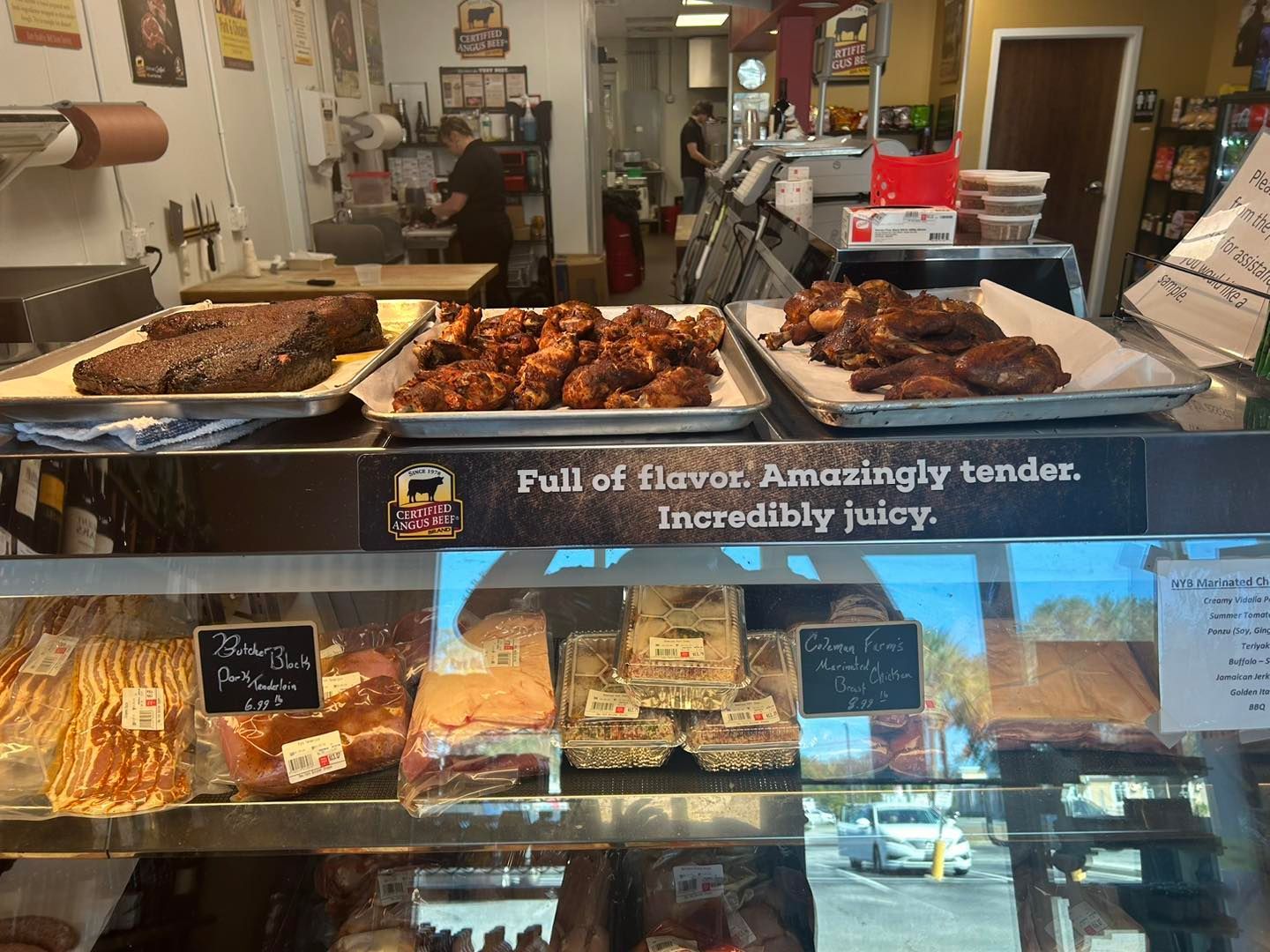 Smoked meats display in a butcher shop: brisket, ribs, and other cuts. Counter display with glass front.