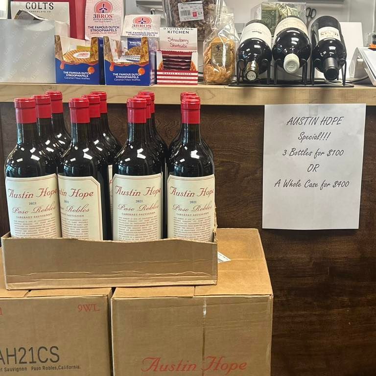 Wine bottles with red caps in boxes; store shelf with a promotion sign.