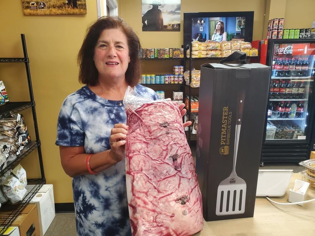 Woman holding a large slab of raw meat next to a boxed grilling spatula in a store.