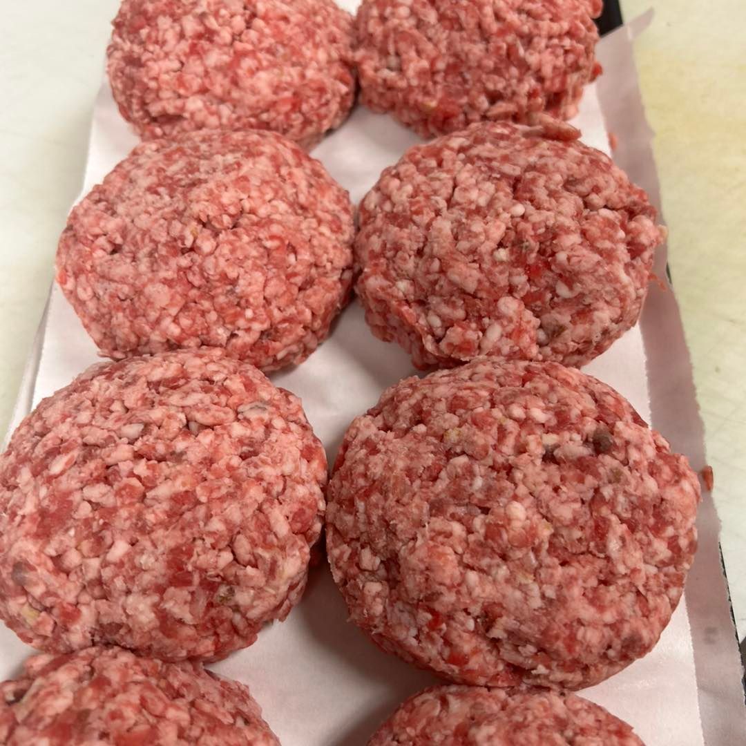 Raw ground beef patties lined up on paper.