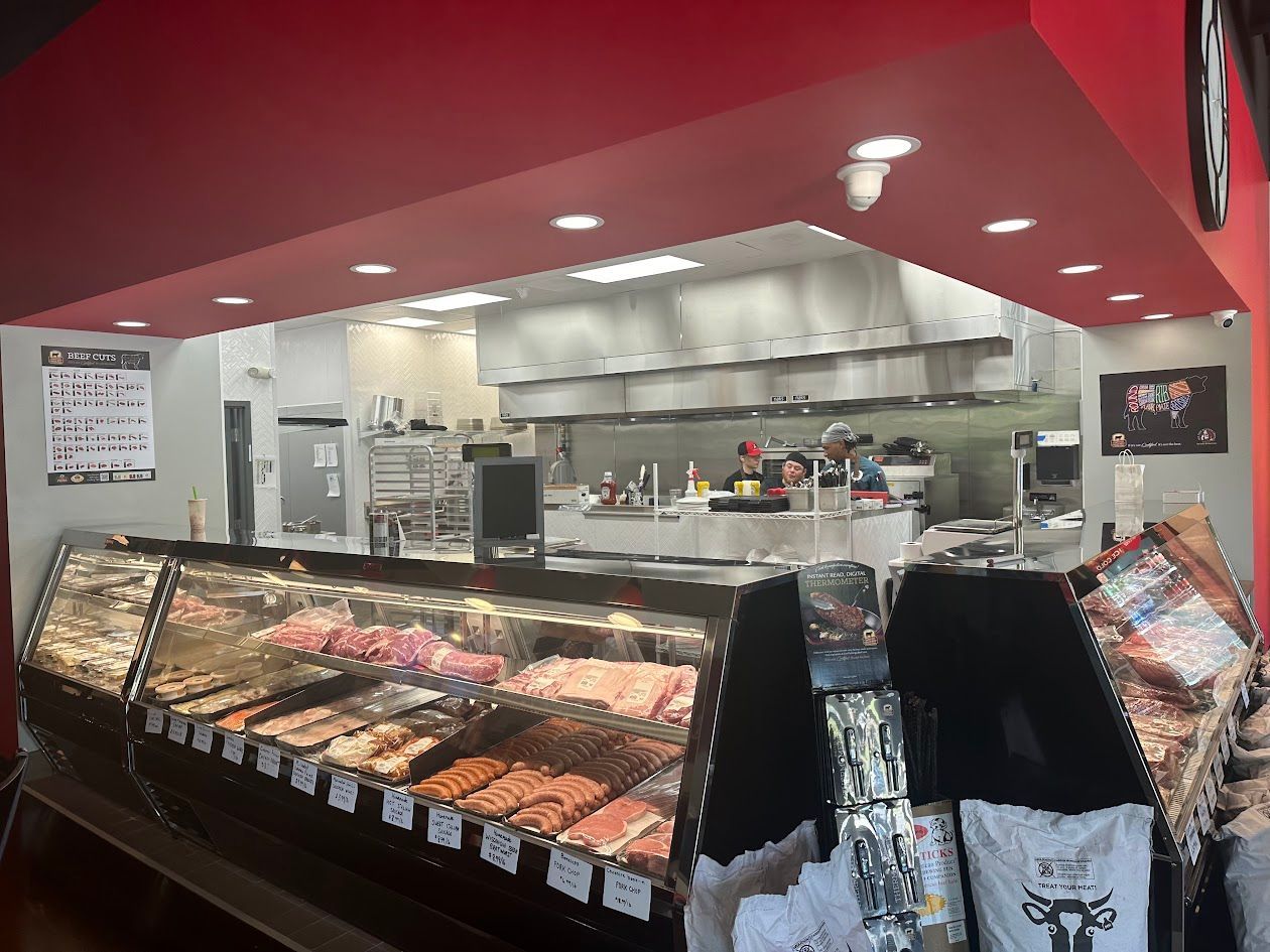 A butcher shop with a display case of meat, behind is a kitchen. Red ceiling, stainless steel appliances.