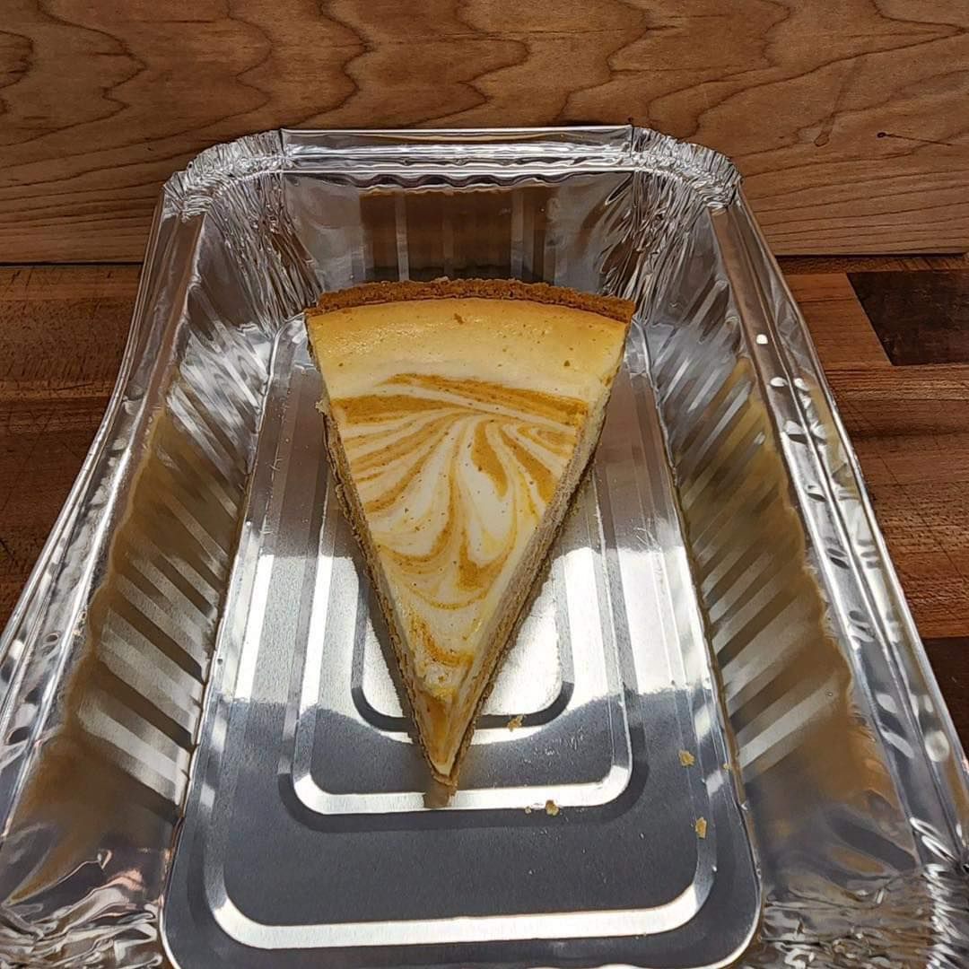 Slice of swirled cheesecake in a silver container on a wooden surface.