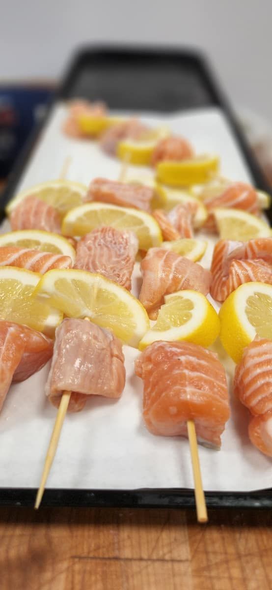 Skewers of salmon and lemon slices on a tray, ready for cooking.