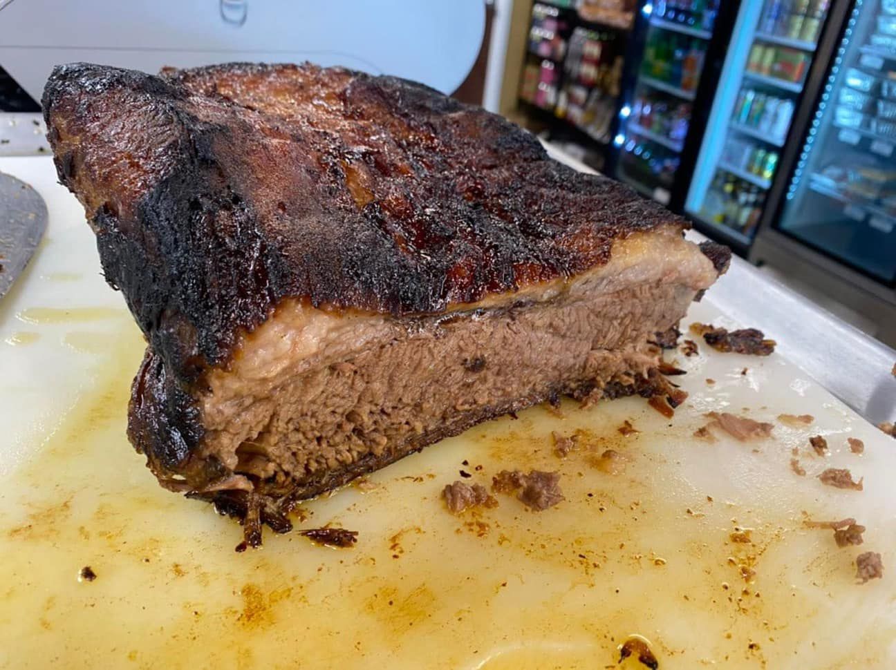 Smoked brisket with dark bark, sliced open, on a cutting board in a store setting.