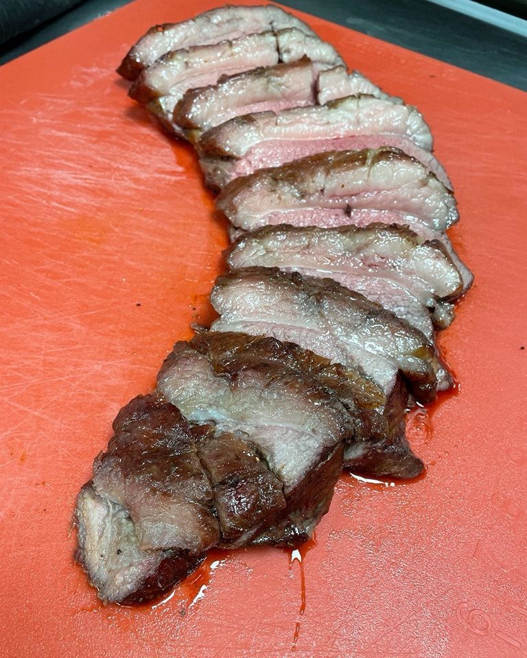 Sliced, seared steak on a red cutting board. Brown crust with pink interior.