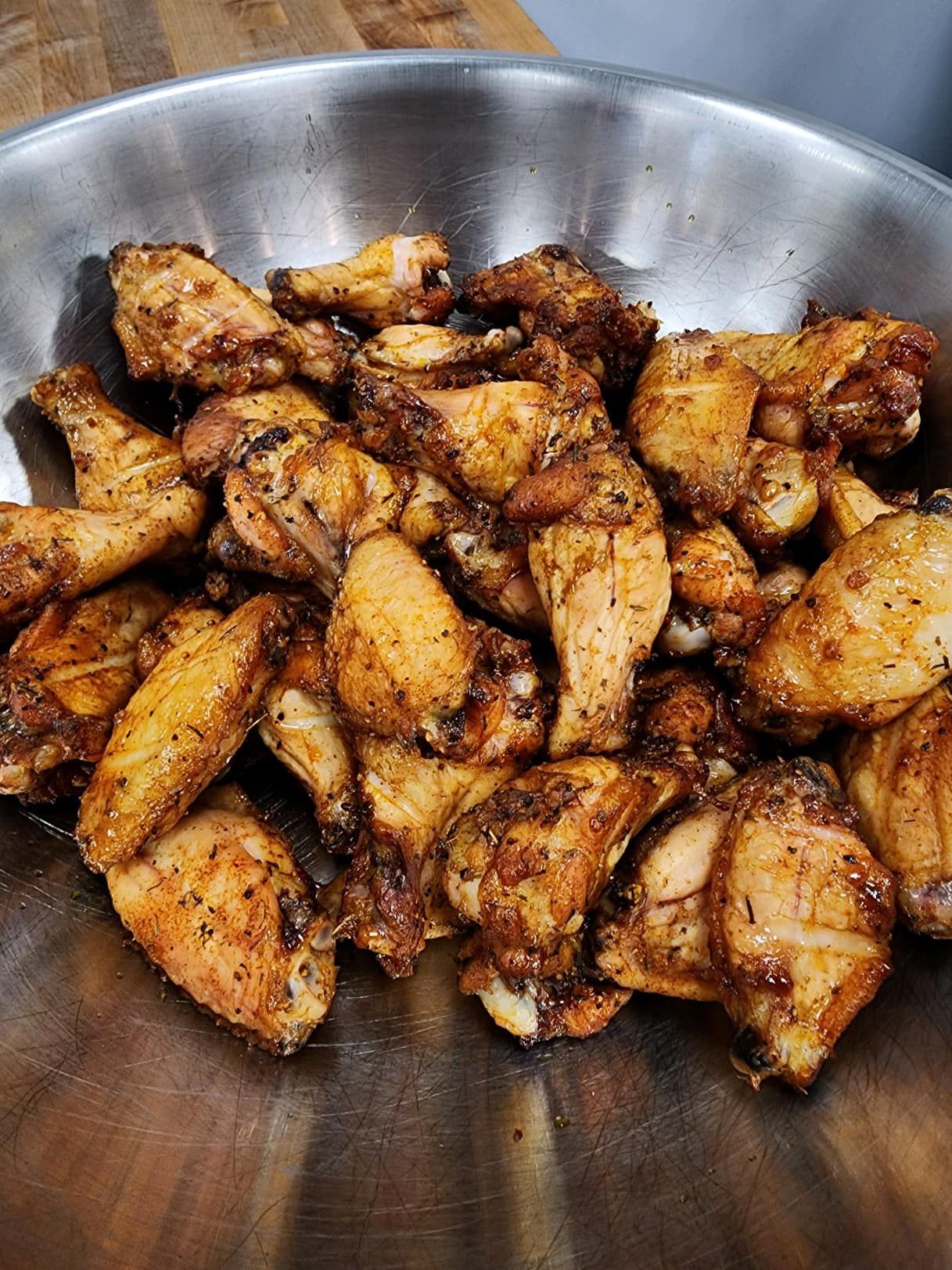A large metal bowl filled with seasoned, golden-brown chicken wings.