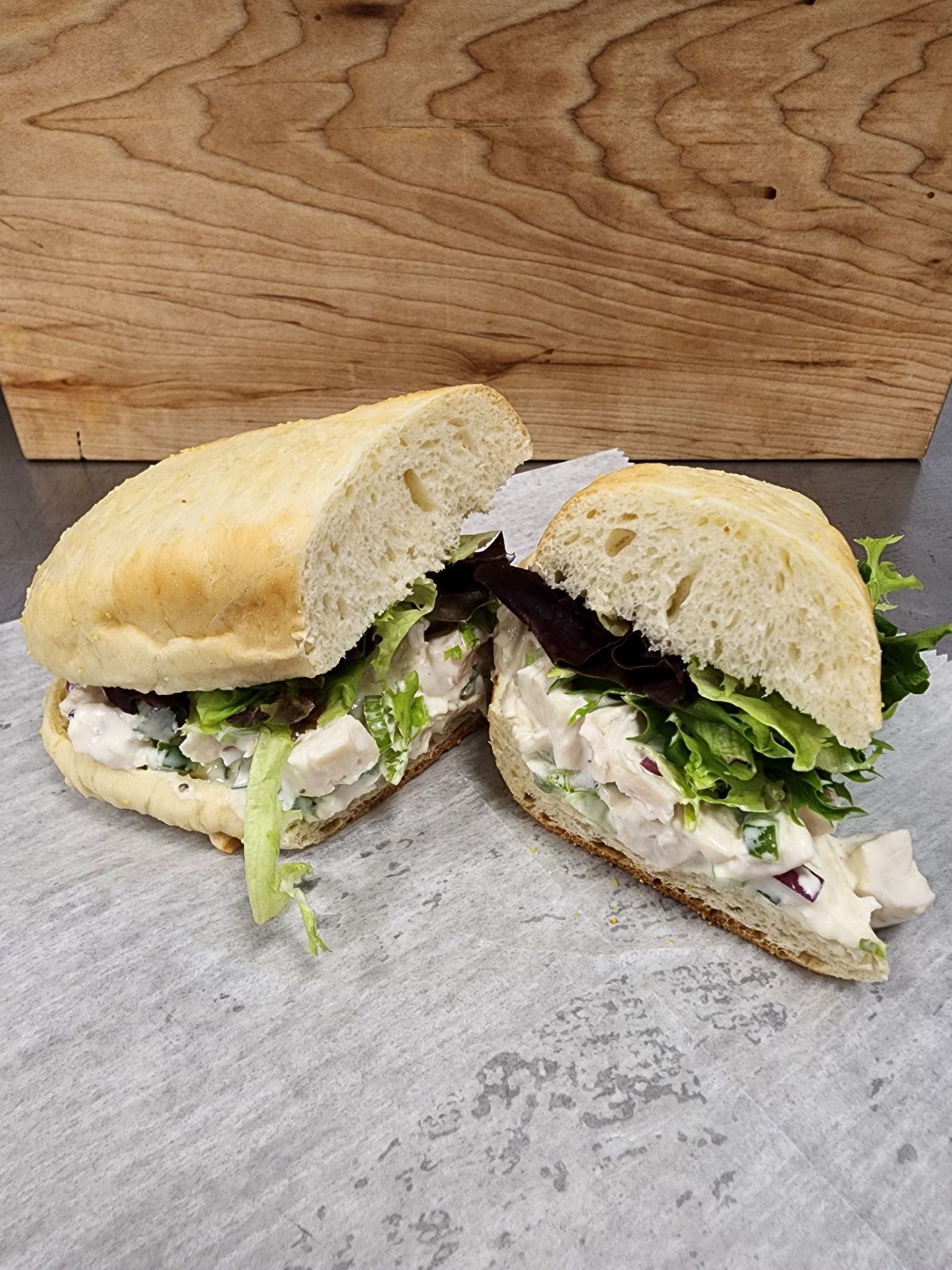 Chicken salad sandwich cut in half, on parchment, lettuce, beige bread.