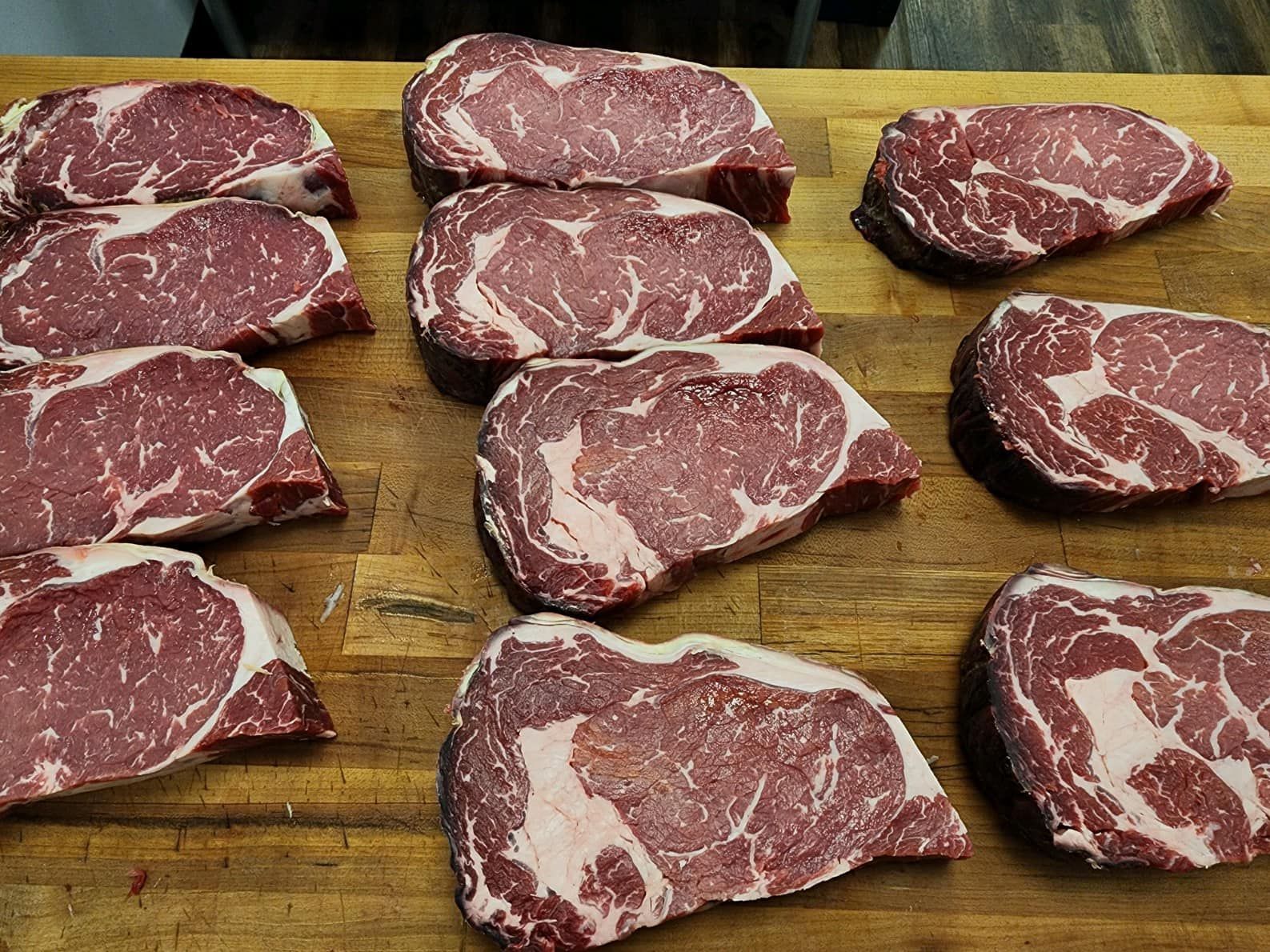 Raw ribeye steaks with marbling on a wooden surface.