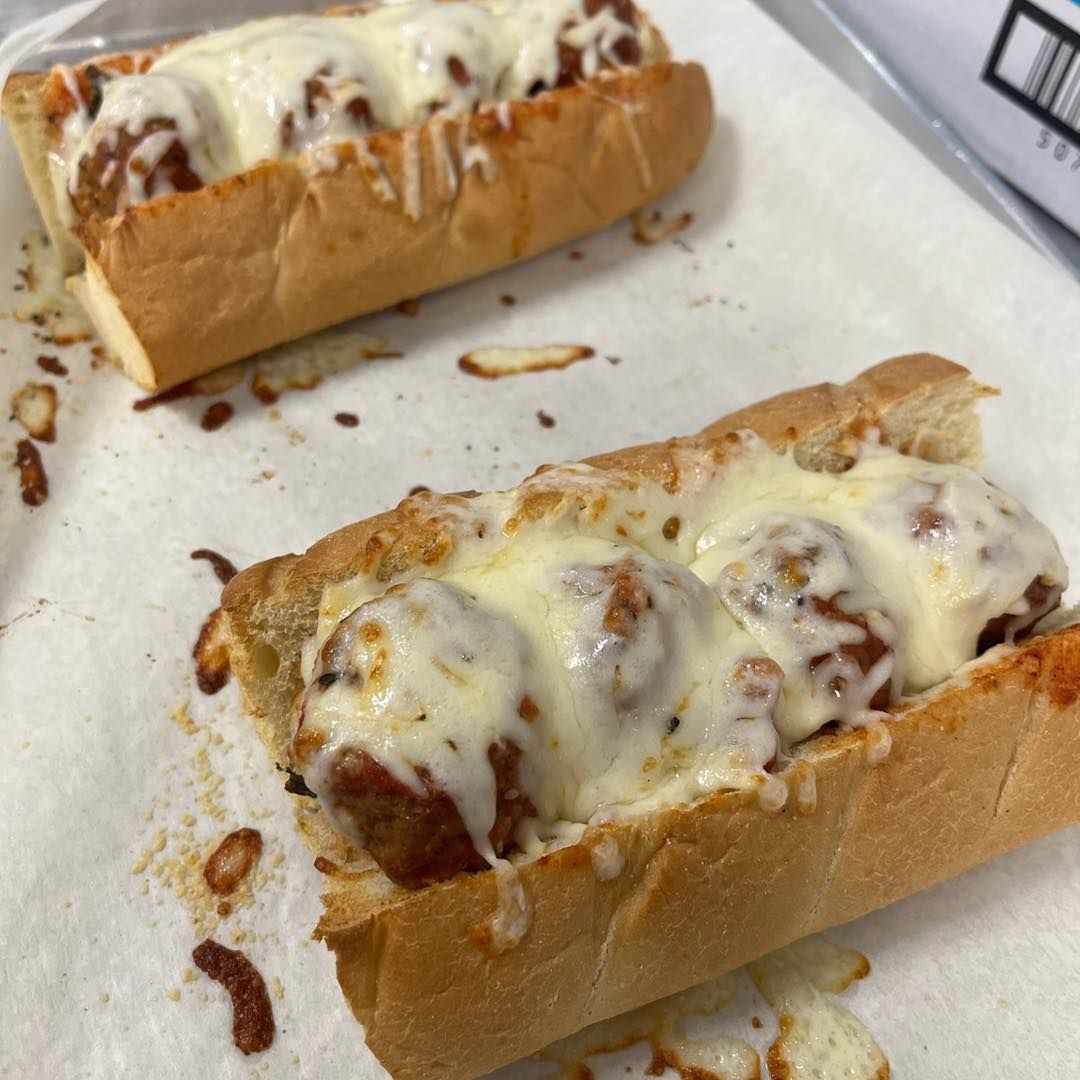 Two meatball subs, covered in melted cheese, on a white surface.