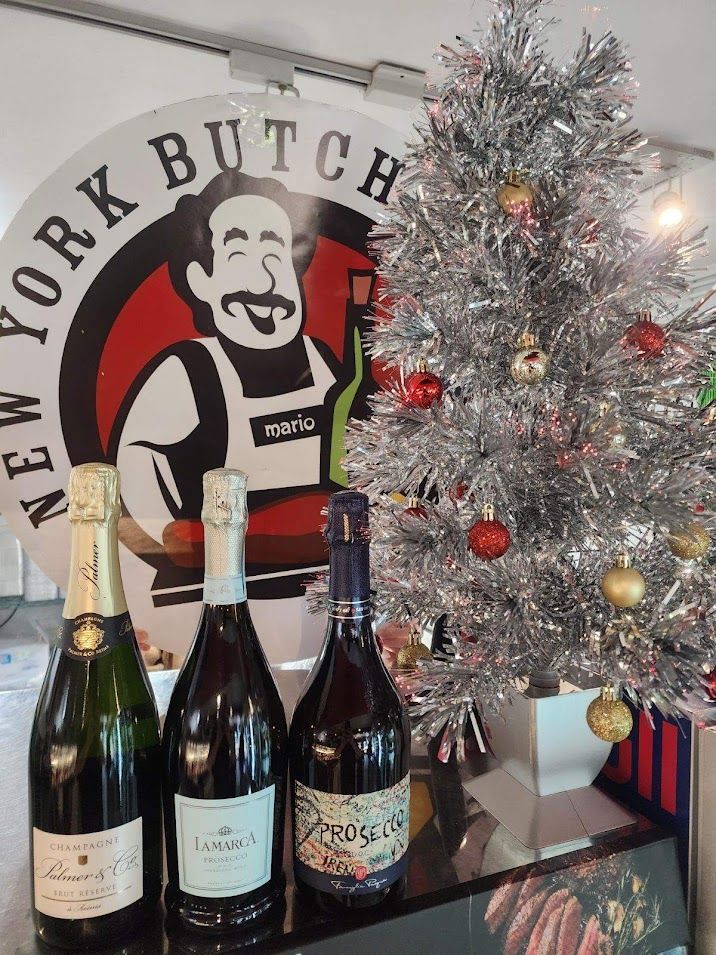 Three wine bottles in front of a shop sign and silver tinsel Christmas tree.