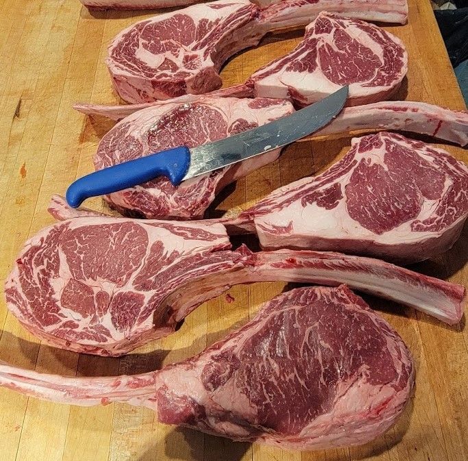 Raw tomahawk steaks with a knife on a wooden surface.