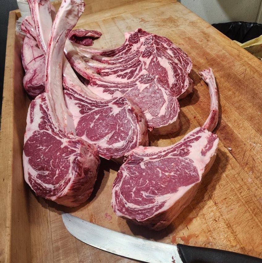 Raw tomahawk steaks on a wooden cutting board with a knife.