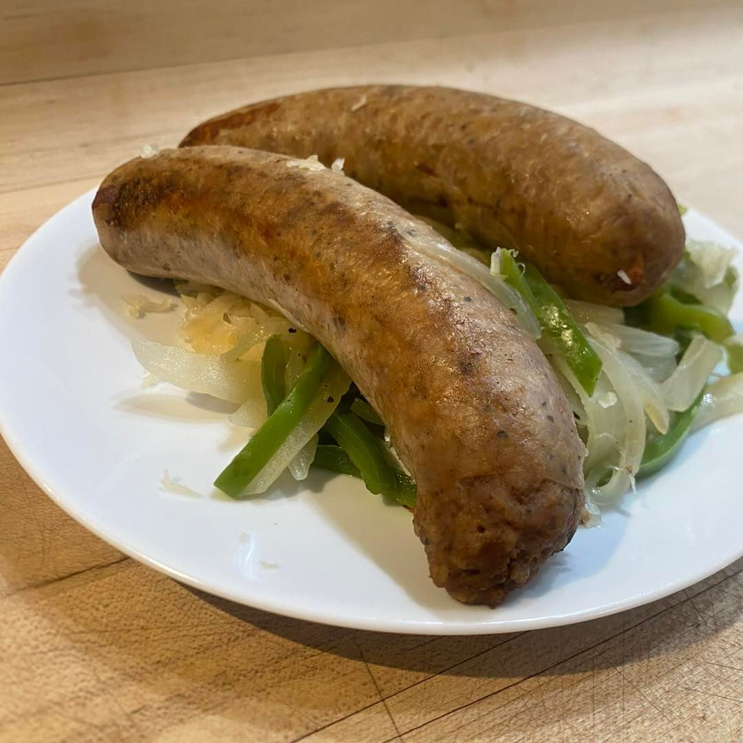 Two browned sausages atop green peppers and onions on a white plate.