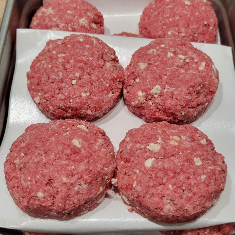 Raw hamburger patties, round and pink, on white parchment in a metal tray.