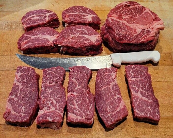 Assorted cuts of raw beef on a wooden surface, next to a knife.