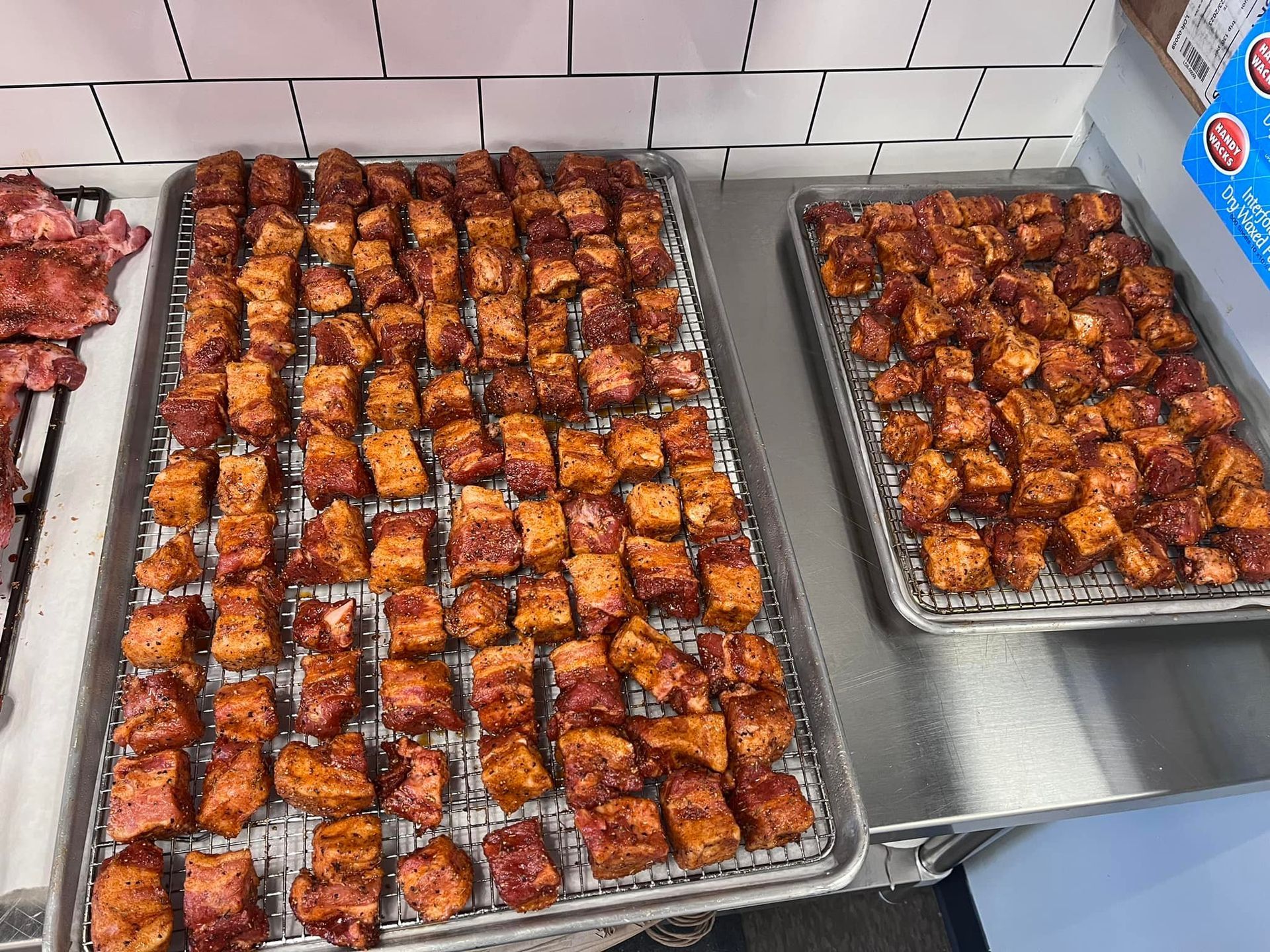 Three trays of cooked, cubed pork belly, glistening with glaze, on a metal counter.