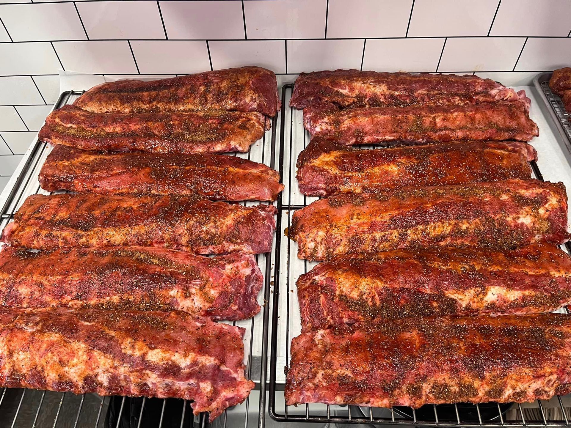Seasoned racks of ribs on cooling racks, ready for cooking.