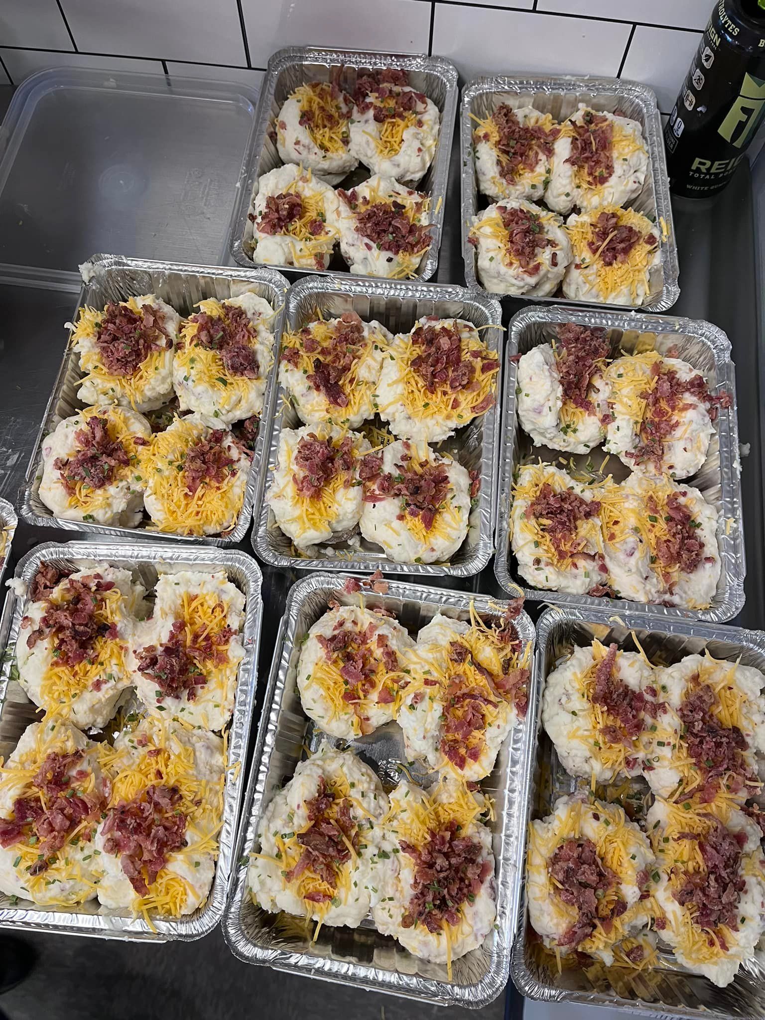 Nine aluminum trays with rice balls topped with yellow and red ingredients, on a table.