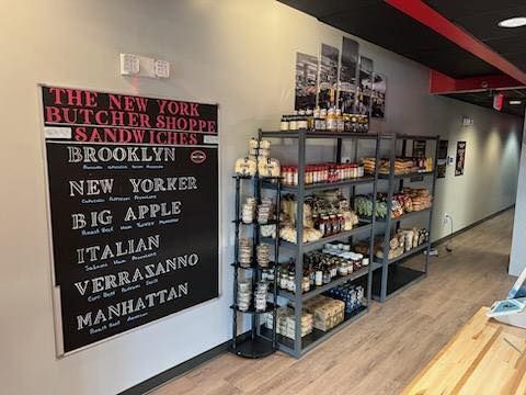 Interior of a shop: chalkboard menu, shelves of goods, black and red accents, and cityscape photos.