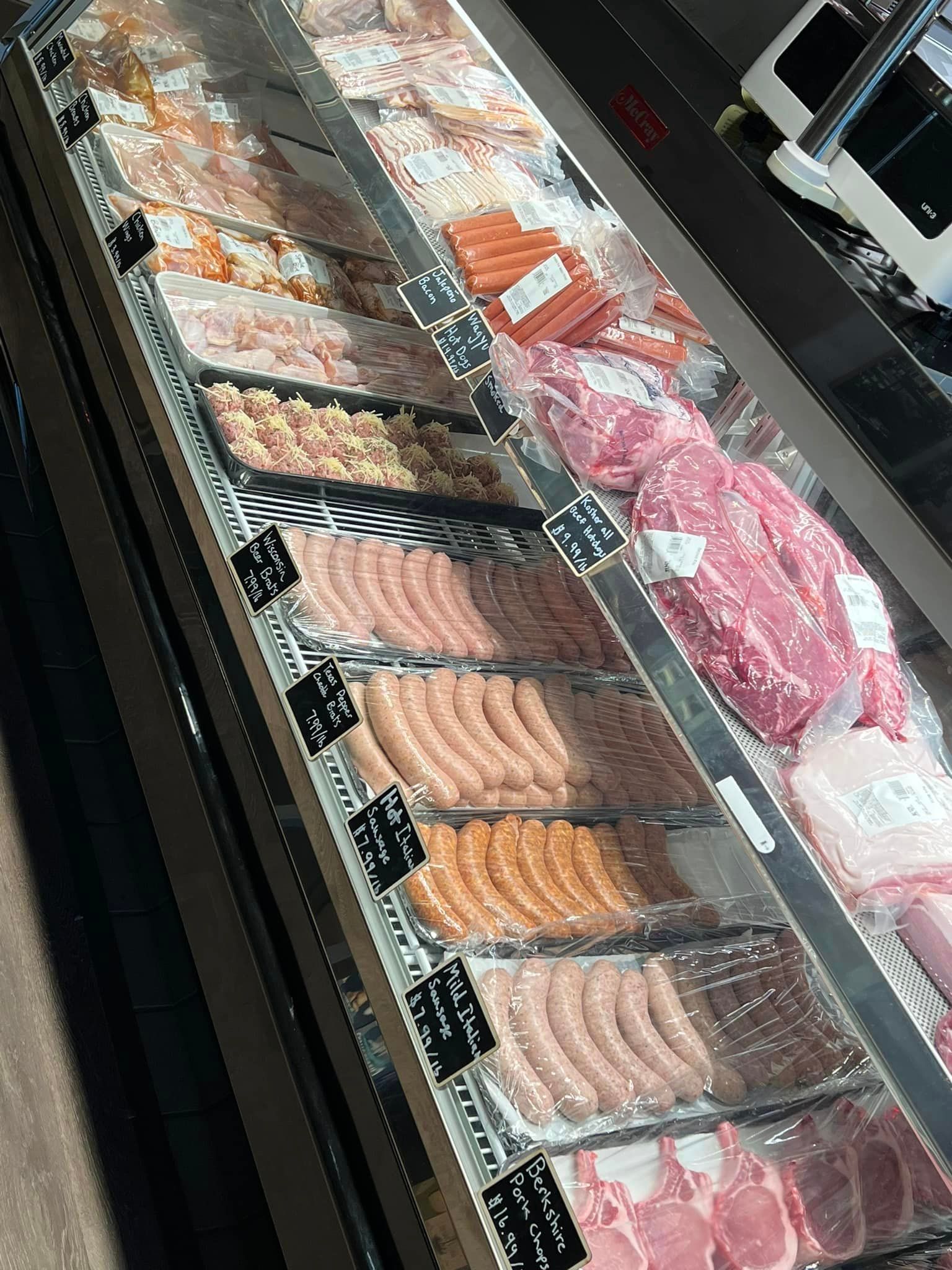 Meat display case in a butcher shop with various cuts, sausages, and packaged items.