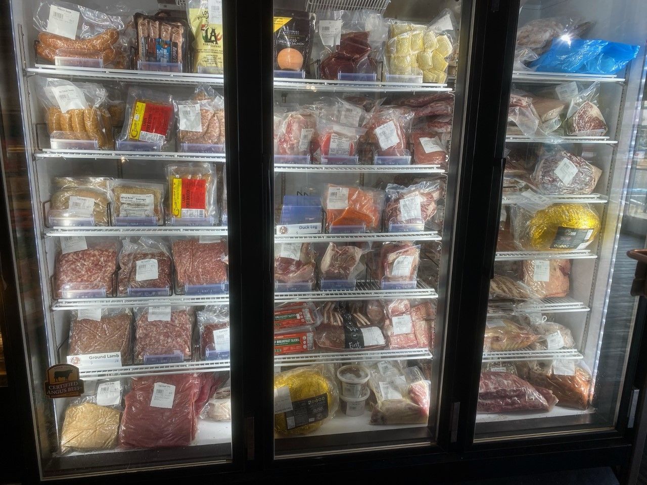 A refrigerated display case filled with packaged meats, sausages, and other food items